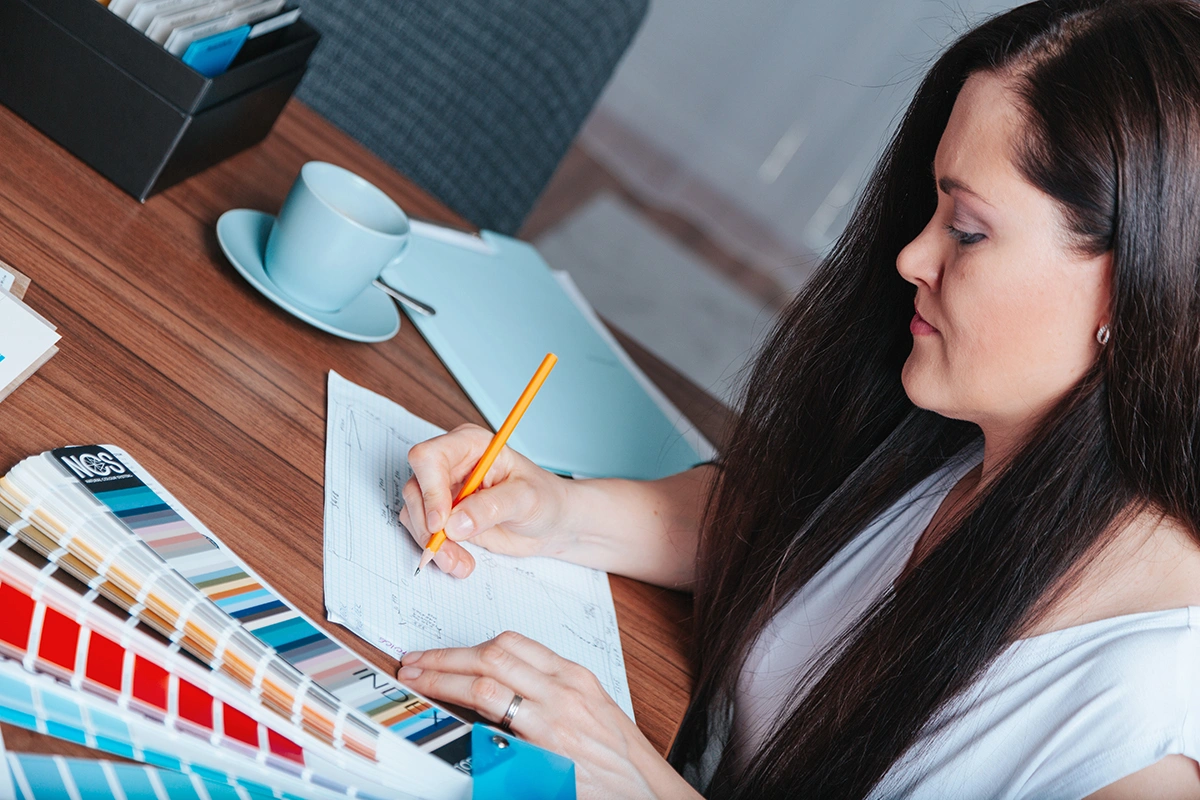 Designérka interiéru pracuje s poznámkami, skicami a vzorníky materiálů u pracovního stolu.